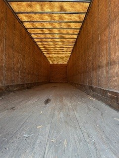 Interior of an empty dry van trailer with wooden side walls and a wooden plank floor, taken from the rear looking forward.