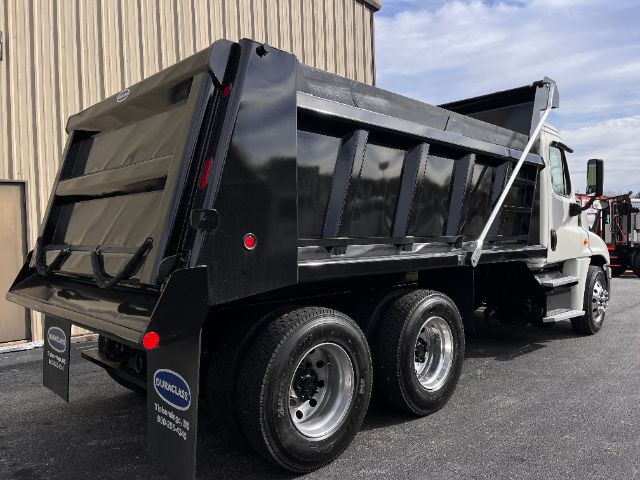 Dump truck with a black dump bed and white cab, Freightliner Cascadia 125 style, rear view showcasing dual rear axles.