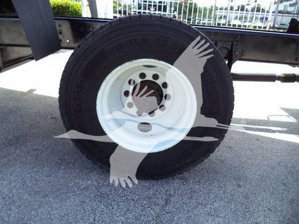 Wheel assembly of a dump truck showing a black tire and white steel rim with bolt holes; tire sidewall text partially visible.