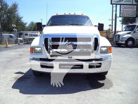 Front view of a white 2015 Ford F650 XLT tow truck with chrome grille and bumper, black mirrors, and large truck headlights.