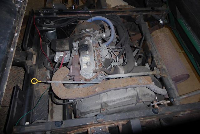 Truck engine bay showing intake manifold, belts, wiring, and rusty exhaust components in a Kawasaki KAF950G engine setup.