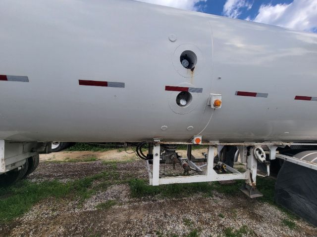 Flatbed side of a cylindrical tanker trailer showing round access ports, hinges, and support frame with a white reflective stripe.