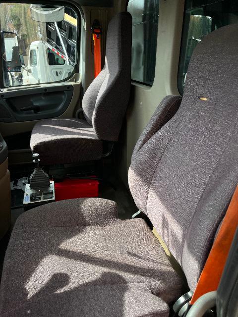 Cab interior of a Freightliner Cascadia truck showing driver and passenger seats, gear shifter, and dashboard area.