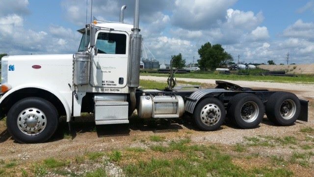 Conventional daycab tractor showing white Peterbilt 379 with twin rear axles and fuel tanks, side view.