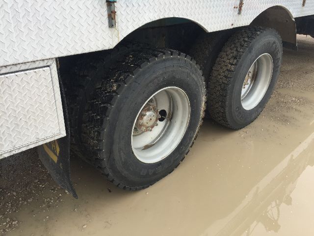 Dual rear wheels of a utility truck with diamond plate side panels; mud and puddles on the ground.