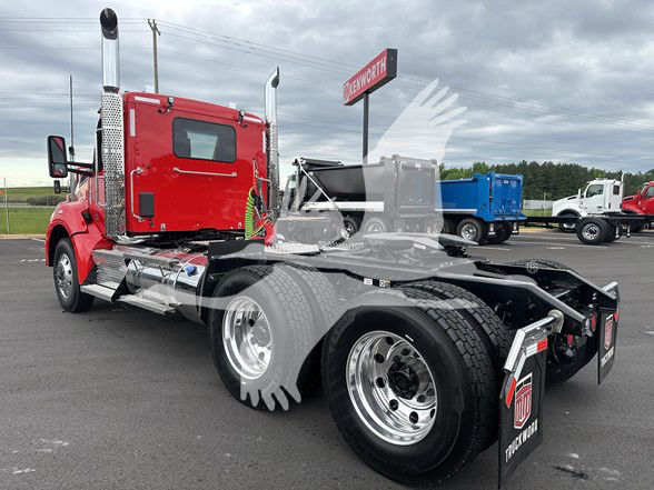 Kenworth T880 tractor cab in red, rear view showing dual rear axles, chrome fuel tanks, exhaust stacks, and fifth wheel mounting area.