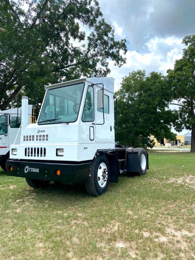 White Ottawa Commando 50 yard truck tractor cab front view, black bumper, large windshield, two mirrors, in a grassy lot with trees.