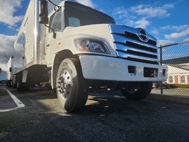 Front view of a white 2025 Hino L6 box truck showing chrome grille, headlights, and front bumper.