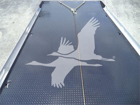 Tractor-trailer or truck bed with diamond plate metal surface and a rope anchor; large bird watermark overlay on the surface.