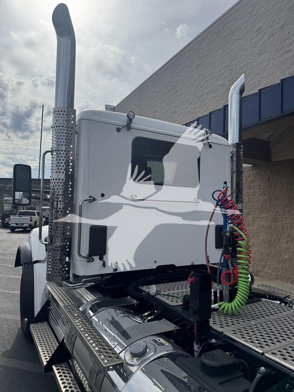 Kenworth T880 truck cab with tall exhaust stacks, chrome air filter, and colorful coiled air hoses in view from the driver side rear.