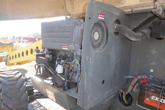 Tractor-style Grove T60 crane chassis showing engine compartment and hydraulic lines with warning labels.