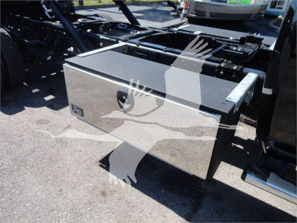 Ram 5500 tow truck chassis with a large aluminum toolbox mounted on the side, undercarriage visible, chrome steps, flatbed frame nearby.