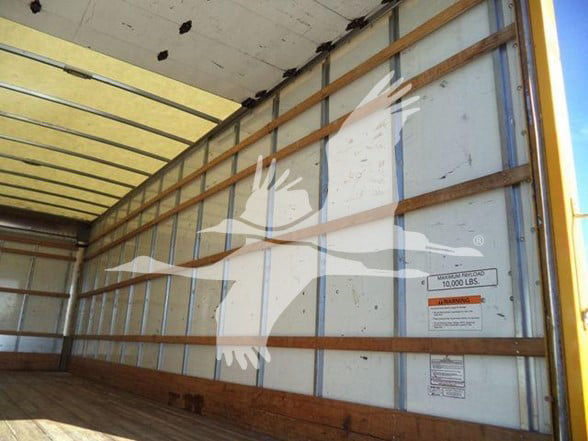 Box truck interior showing sidewall with large white graphic dolphin or abstract design; metal ribs and wooden floor; warning label and capacity placard visible.