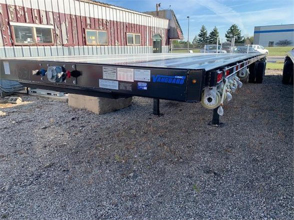 Flatbed trailer with Vanguard branding showing control valves and labels on the front edge; visible text includes VANGUARD and various small sticker labels.