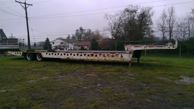 Trail King TK70HT-482 lowboy trailer in-side view showing long flatbed with triangular cutouts along side and hitch at front.