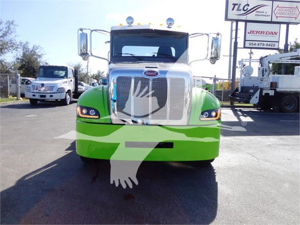 Front view of a green and white 2022 Peterbilt 337 tow truck with chrome grille and headlights, large side mirrors, and a dealership lot in the background.