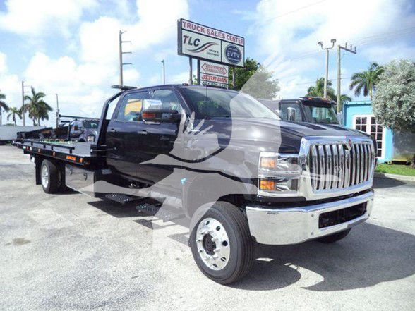 Truck in a dealership lot showing 2023 International CV tow truck with flatbed and chrome front grille.