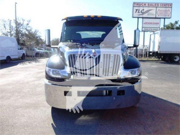 Truck front view showing large chrome grille, bumper, and headlights. Visible signs in background read 'TRUCK SALES CENTER' and logos. License area obscured by watermark.