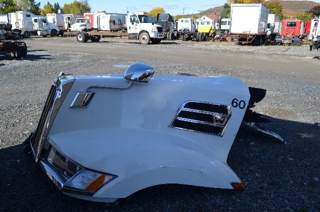 Truck cab exterior piece with white paint, side mirrors, grille, and number 60 visible along the side; background shows a yard with many trucks.