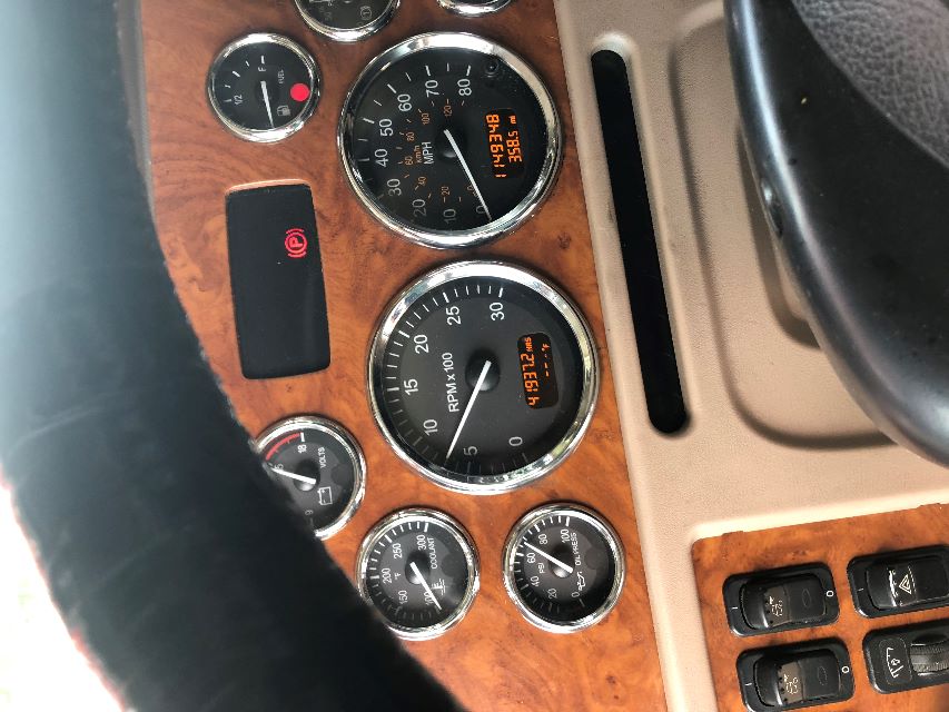 Truck dashboard with wood-grain panel, showing multiple gauges: RPM x100 (center), MPH (right), coolant gauge (left), oil pressure gauge (bottom left), fuel gauge (top right). An orange digital odometer reads 149,34? and 358.5 mi. Hazard sw