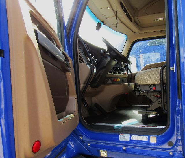Truck cab interior showing steering wheel and driver seat in a blue Kenworth cab chassis, with tan interior and dashboard visible.