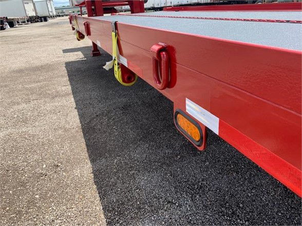 Flatbed trailer side with red drop deck, reflective markers, and tie-down rings along the edge.