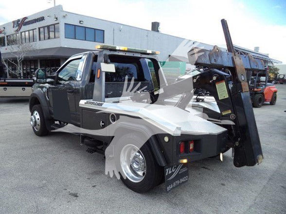 Tow truck rear view with hydraulic lift, 2017 Ford F-450 with flatbed and crane in tow configuration.