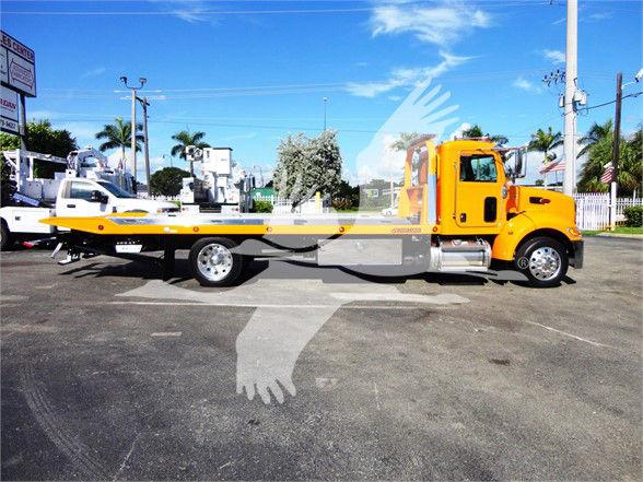 Peterbilt 337 tow truck with orange cab and flatbed, side view on pavement.