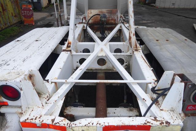 trailer chassis and framing of a Fruehauf pneumatic dry bulk trailer showing rusty spots and white paint, rear view with cross-braced structure and discharge chute