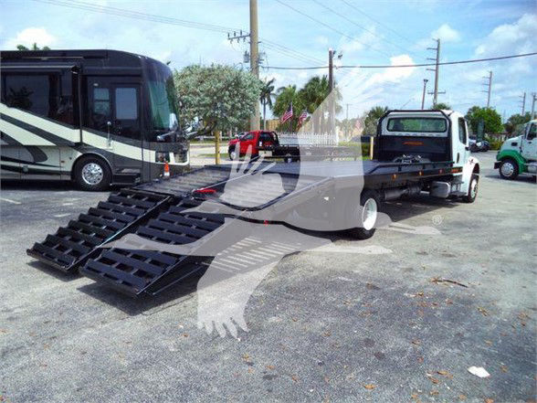 Flatbed tow truck with a ramp system attached, Freightliner Business Class M2 106-style scene in a parking lot.