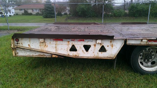 Trail King TK70HT-482 lowboy trailer side undercarriage with rust and triangular cutouts on white metal frame.