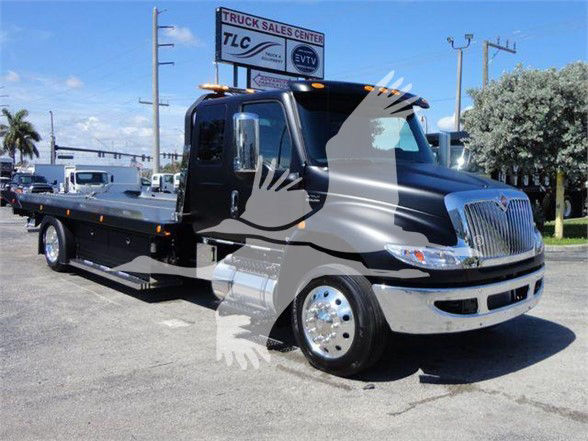 Tow truck chassis showing cab with chrome front grille and flatbed, International MV style, dealership lot in background.