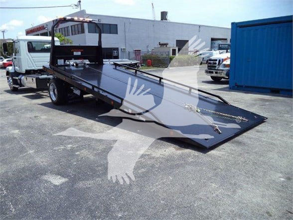 Flatbed tow truck with a long black platform, showing a raised incline ramp and side rails.