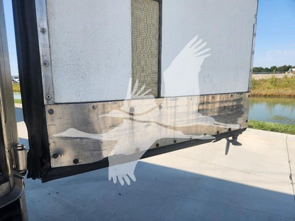 Trailer rear corner with metal panels, riveted frame, and a faded large graphic of a bird with wings spread across the lower portion of the door. Visible text not discernible.