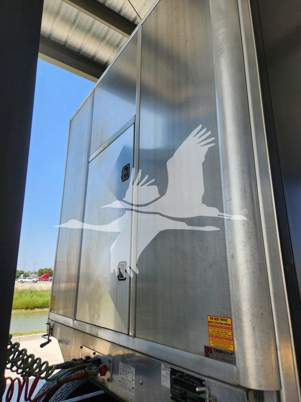 Curtainside trailer side with large white seagull logo on silver metal panel, access doors and warning label visible.