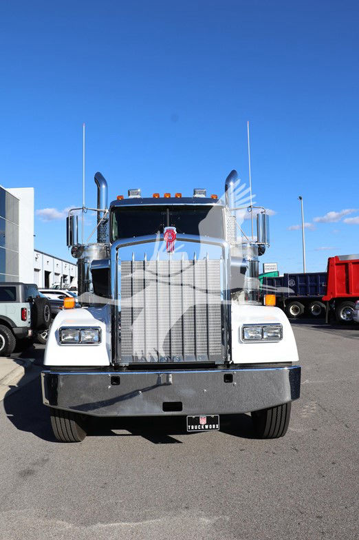 Front view of a white Kenworth W900L conventional truck with chrome grille, large bumper, and dual exhaust stacks; badge and lights visible.