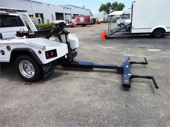 Ram 4500 tow truck with hitch attachment and extended boom for lifting, visible in a lot with other trucks and equipment.