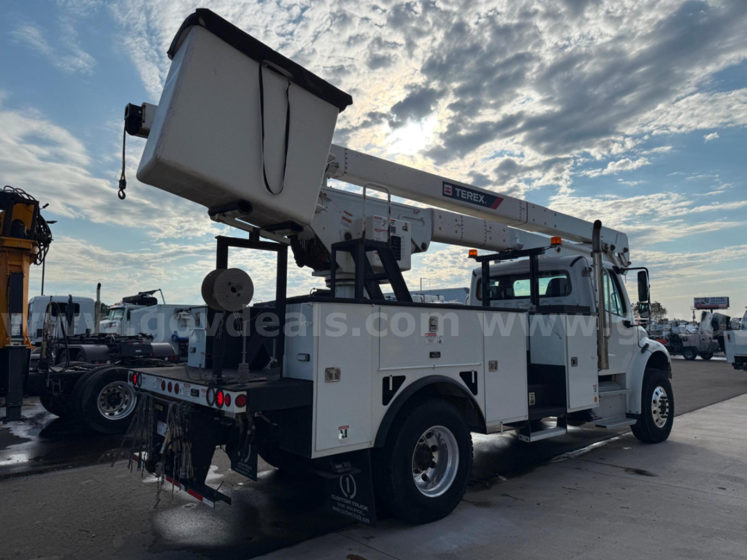 Bucket truck with boom lift extended, Freightliner TEREX TC-55, utility body with compartments, in a dealership lot.