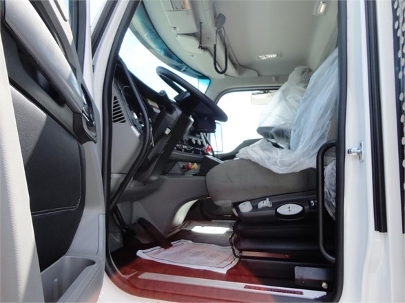 Truck cab interior showing steering wheel, dashboard, driver seat with plastic cover, and entry area. Visible components include pedals, floor mat, and control panels.
