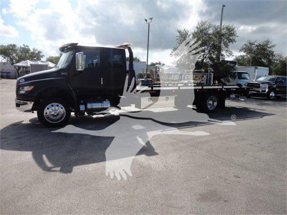 Tow truck with dark cab, flatbed, and chrome wheels. Text and branding not clearly legible on the image.