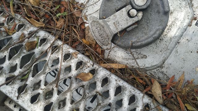 Image shows a close-up of a circular lock/hasp and key on a metallic surface with a perforated grate and debris; part of a Peterbilt 386 truck.