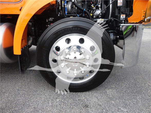 Front wheel and suspension of a 2022 Peterbilt 337 tow truck with chrome hub and black tire; engine bay visible in background.