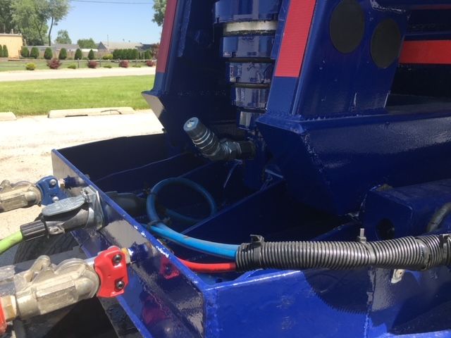Blue 2006 utility dump trailer with hydraulic ram and hoses, showing connection fittings and control valve at the rear corner.