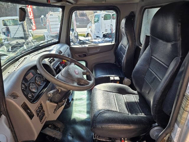 Truck cab interior with steering wheel, dashboard gauges, and black vinyl seats in a Peterbilt 348 cab.