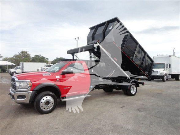 Ram 5500 SLT truck with a large black hooklift bed in elevated position, red cab, no visible text on the vehicle.