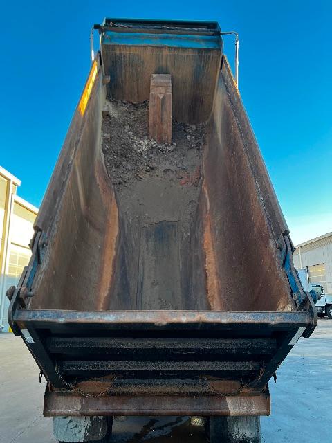 Dump truck bed with reinforced steel walls and hopper, showing interior load area and a wooden stake at the bottom.