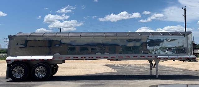 2025 aluminum end dump trailer side view with dual rear axles and support legs, reflective side panels, and black-tinish coating.