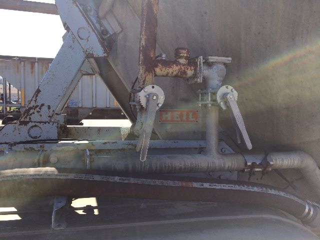 Trailer hitch area of a pneumatic dry bulk trailer with metal handles and rusted fittings, label reading 'HEIL' on side of tank.