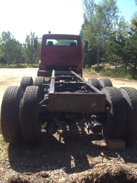 Truck chassis with six wheels visible, diesel engine bay area, various components, Freightliner cab at right side.