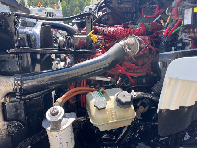 Engine bay of a 2015 Freightliner M2 cab and chassis showing coolant reservoir, large black radiator hose, red engine block, and various hoses and wiring.